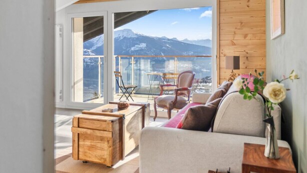 Ein modernes Interieur mit einer Couch, einem Holztisch und Blick auf Berge durch große Fenster.