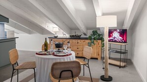 Ein Essbereich mit einem runden Tisch für vier Personen, einem Fernseher auf einem Schrank und einer Küche im Hintergrund.