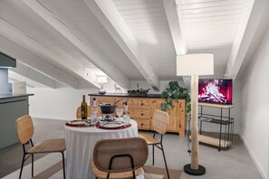 Ein Essbereich mit einem runden Tisch für vier Personen, einem Fernseher auf einem Schrank und einer Küche im Hintergrund.
