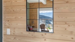 Ein Zimmer mit Holzwänden, einem großen Fenster, einem Stuhl, einem kleinen Tisch und Blick auf Berge.