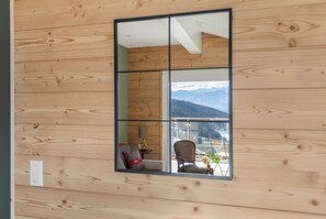 Ein Zimmer mit Holzwänden, einem großen Fenster, einem Stuhl, einem kleinen Tisch und Blick auf Berge.