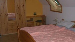 Makuuhuoneessa on kerrossänky, työpöytä tuolilla, pieni kasvi, lamppu ja sänky, jossa on vaaleanpunainen peitto.