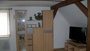 Huoneessa on puinen kaappi, jalustalla oleva televisio ja patteri.