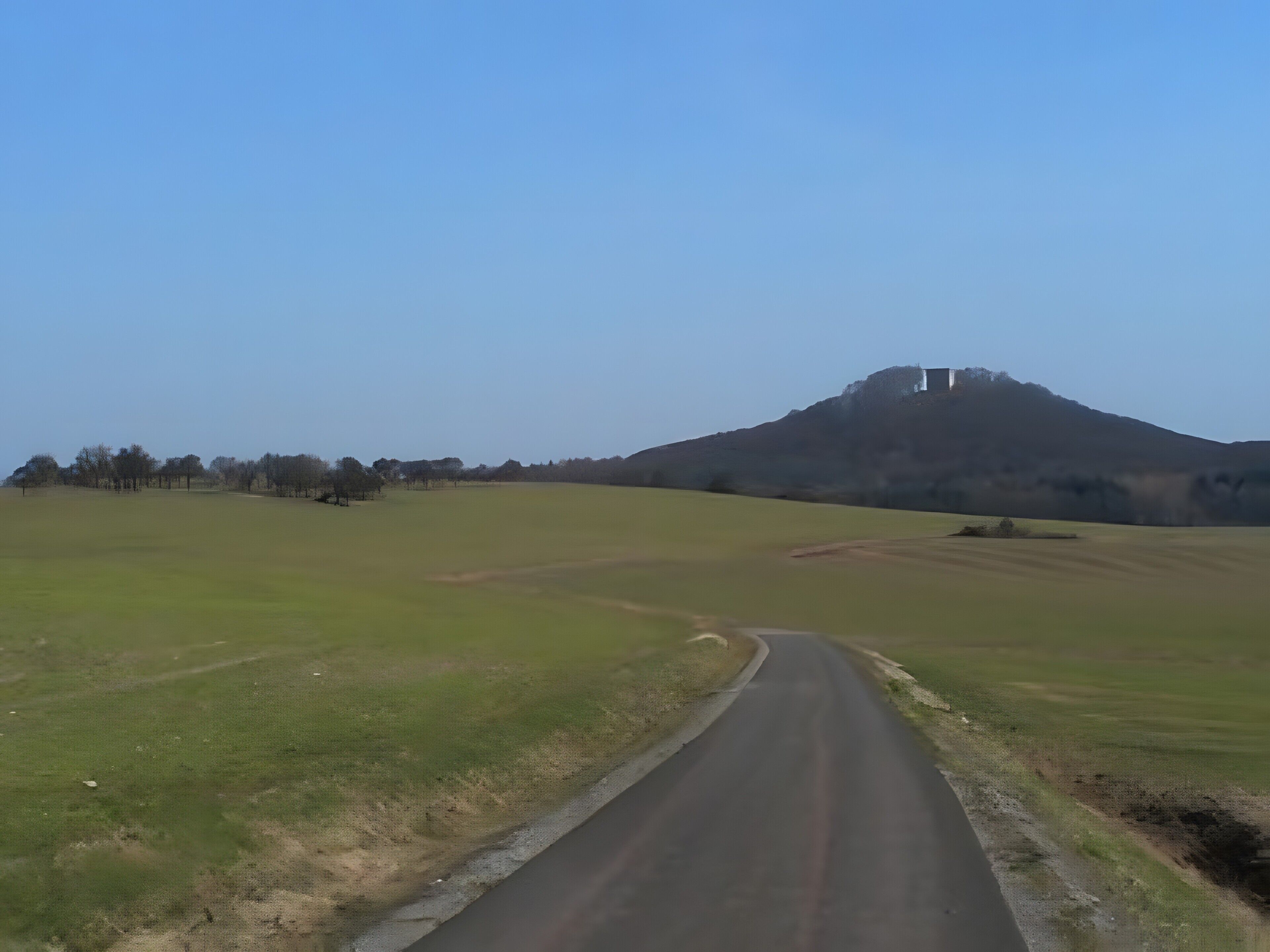 Une route de campagne menant à une colline sur laquelle se trouve une construction.