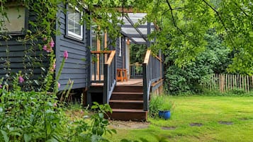 A wooden deck with a staircase leading to a covered porch, surrounded by lush greenery.