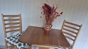 A wooden dining table with a vase of dried flowers, two wooden chairs with patterned cushions, and a wooden floor. - Sheperd's Hut, Sleeps 2 With Hot Tub and Garden (Glengarriff)