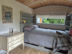 Un dormitorio con cama, escritorio con cajones, espejo, estanterías y ventana con vista a follaje.