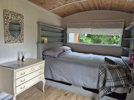 Un dormitorio con cama, escritorio con cajones, espejo, estanterías y ventana con vista a follaje.