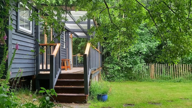 A wooden staircase leading to a covered porch with a view of a lush garden. - Sheperd's Hut, Sleeps 2 With Hot Tub and Garden (Glengarriff)