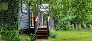 A wooden staircase leading to a covered porch with a view of a lush garden.