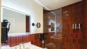 A bathroom with a large mirror, a sink with two faucets, a toilet, and a shower area with a glass door.