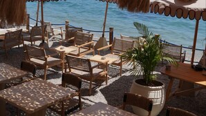 Outdoor seating with umbrellas, a potted plant, and a view of the sea and boats.