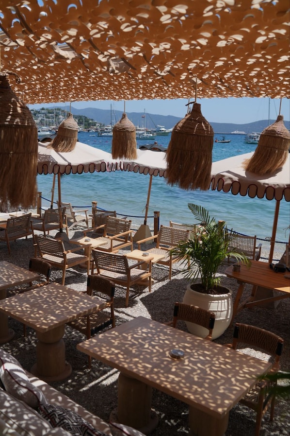 Outdoor seating with umbrellas, a potted plant, and a view of the sea and boats.