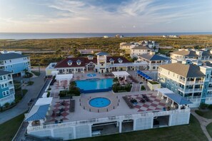 Ein Resort mit mehreren Gebäuden, einem zentral gelegenen Pool und Blick auf den Strand.