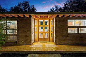 Un bâtiment à la façade en briques, doté de grandes fenêtres et d’une porte d’entrée en bois située au centre.