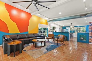 Un espace de vie moderne comprenant un canapé, une table basse et des fauteuils, une cuisine avec un mur d’accent bleu et un ventilateur de plafond.