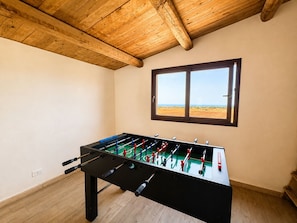 Una habitación con mesa de futbolín, vigas de madera en el techo, una ventana con vistas y un interruptor de luz en la pared.