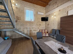 Ein Zimmer mit Steinwand, einer Holztreppe, einem an der Wand befestigten Fernseher und einem Essbereich mit Tisch und Stühlen.