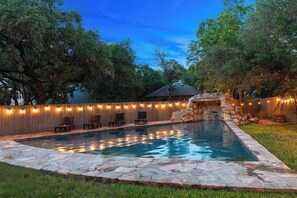 Ein Garten mit Swimmingpool, Steinbordurad, Holzliegen und Lichterketten.