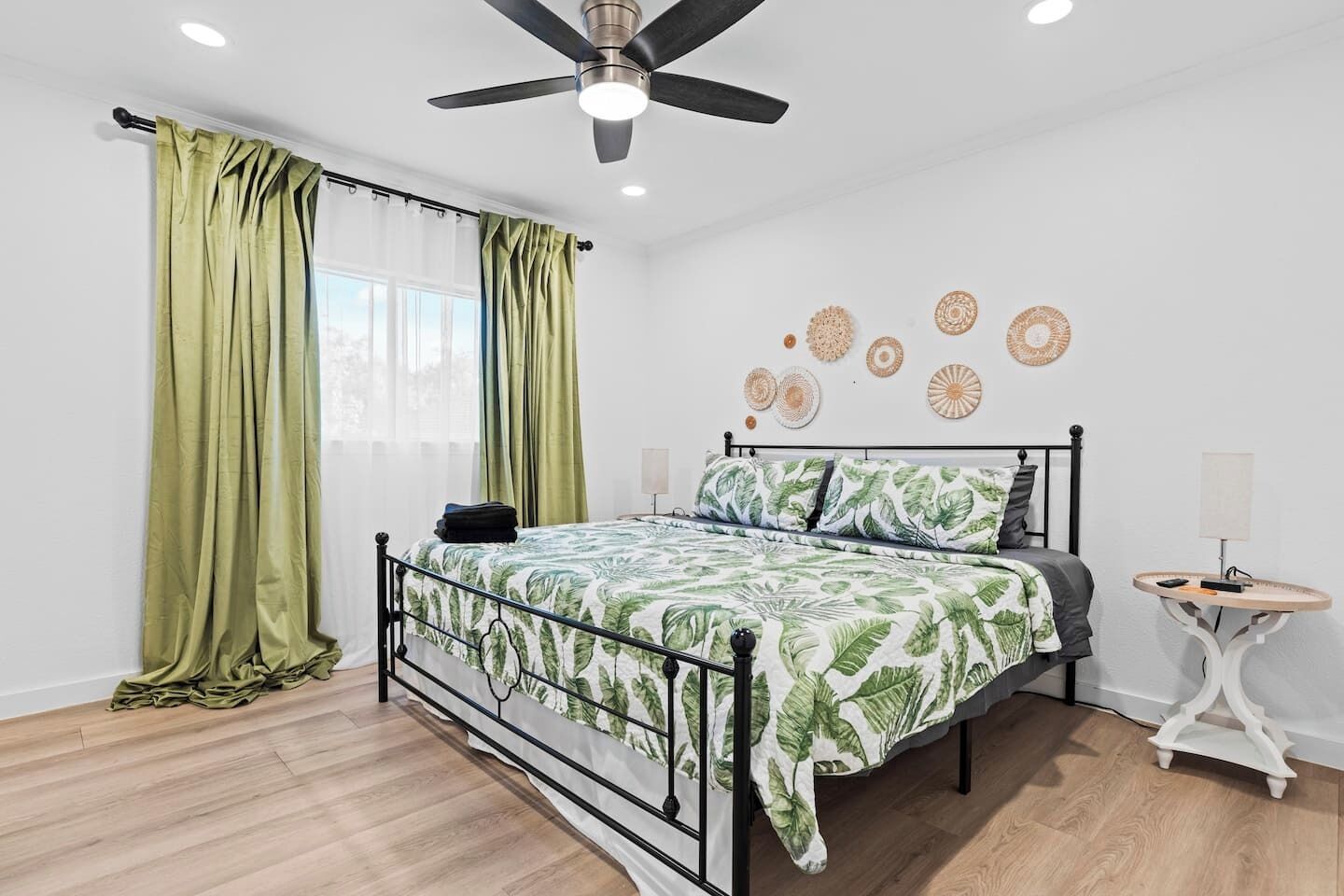 Un dormitorio con cama, ventilador de techo, ventana con cortinas y decoración en la pared.