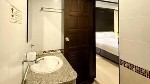Un baño con lavamanos, espejo, perchero para toallas y una puerta que da al dormitorio.