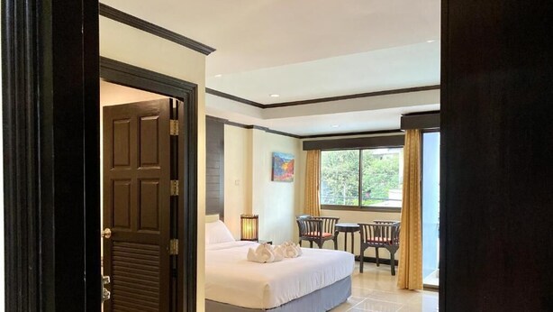 Una habitación de hotel con cama, una pequeña mesa con sillas, una ventana con cortinas y una puerta.