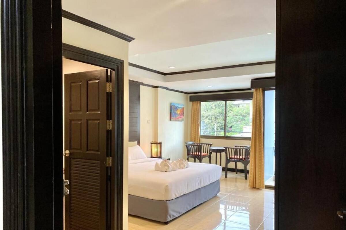 A hotel room with a bed, a small table with chairs, a window with curtains, and a door.