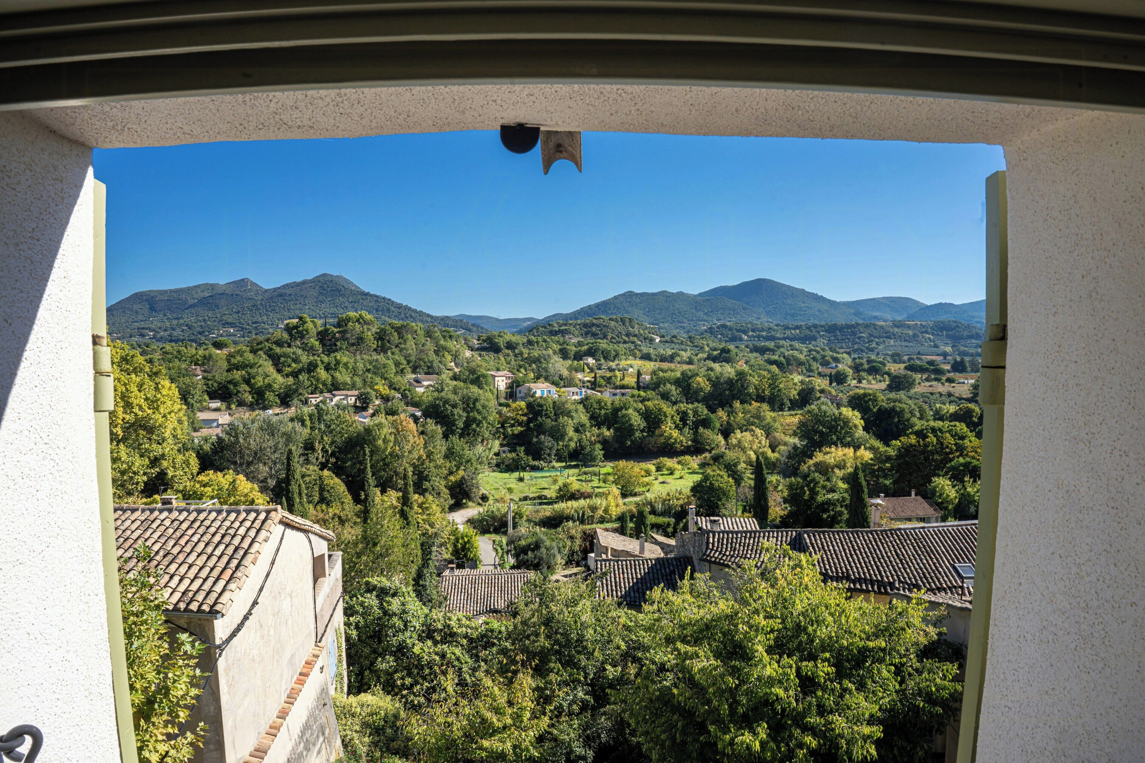 Vista desde una ventana sobre un pueblo con edificios tradicionales y montañas al fondo.