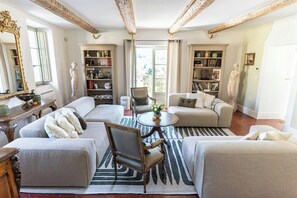 Ein geräumiges Wohnzimmer mit einer Sofagarnitur, einem runden Couchtisch und zwei Bücherregalen, gefüllt mit Büchern und dekorativen Gegenständen.
