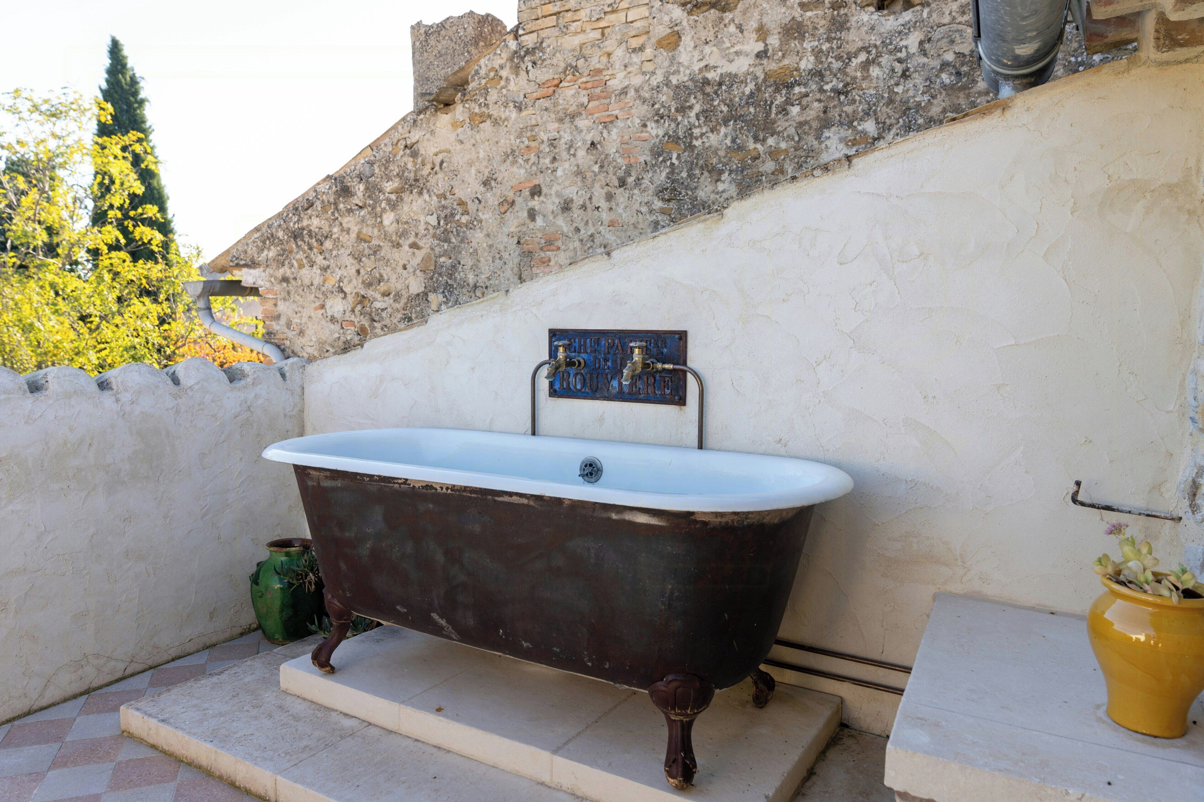 An outdoor bathtub with a metal plaque, a green pot, and a yellow pot on a stone ledge.