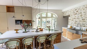 Una cocina moderna con una isla grande, sillas de mimbre, luces colgantes y una pared de piedra.