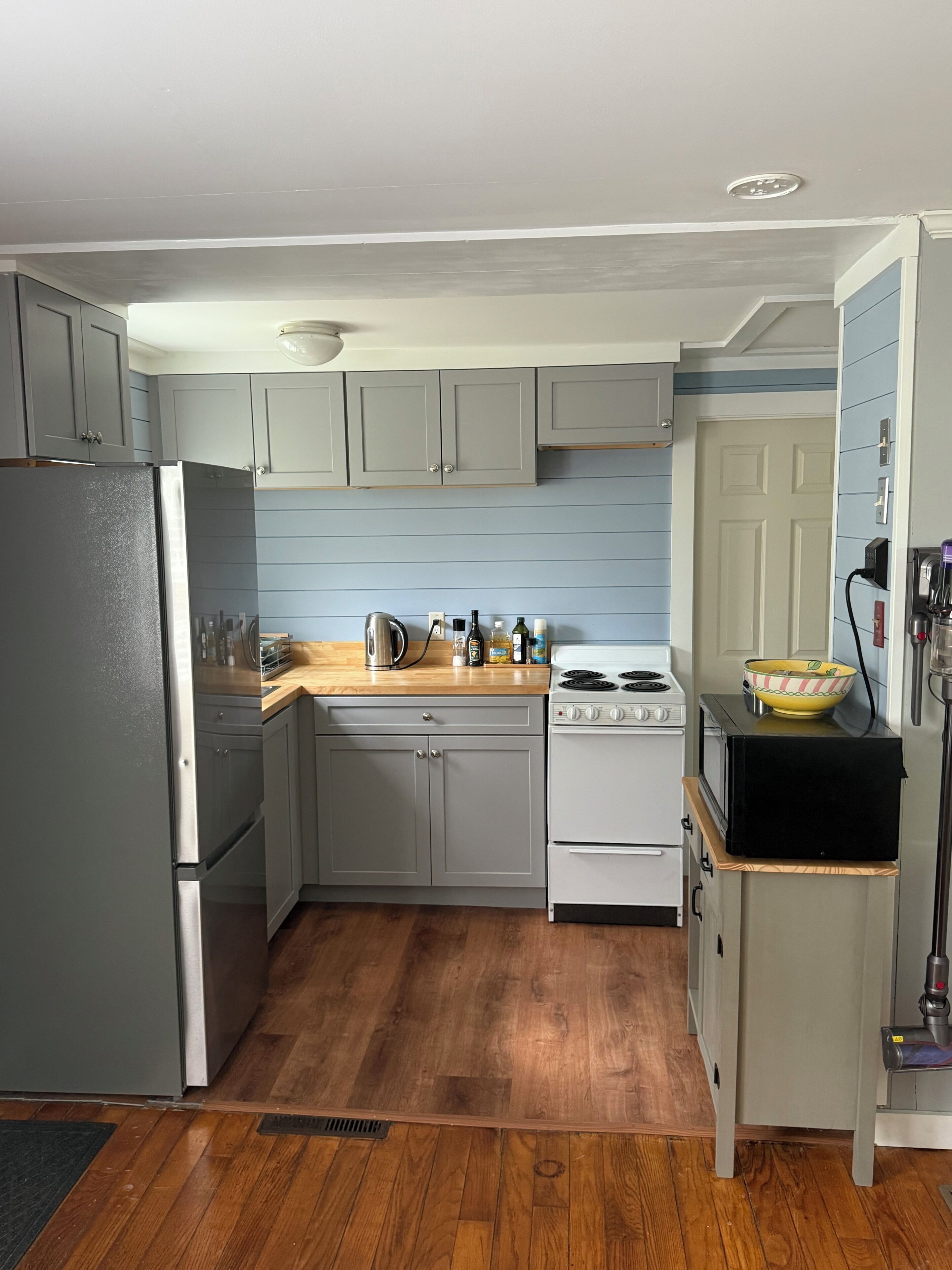 Una cocina con armarios grises, una encimera de madera, un refrigerador de acero inoxidable, una estufa y un microondas.