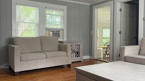 A bedroom with a wooden floor, a beige sofa, a white bed, and a cabinet. - Charming 2 bedroom cottage by the pond in Eastham, Cape Cod (Eastham)