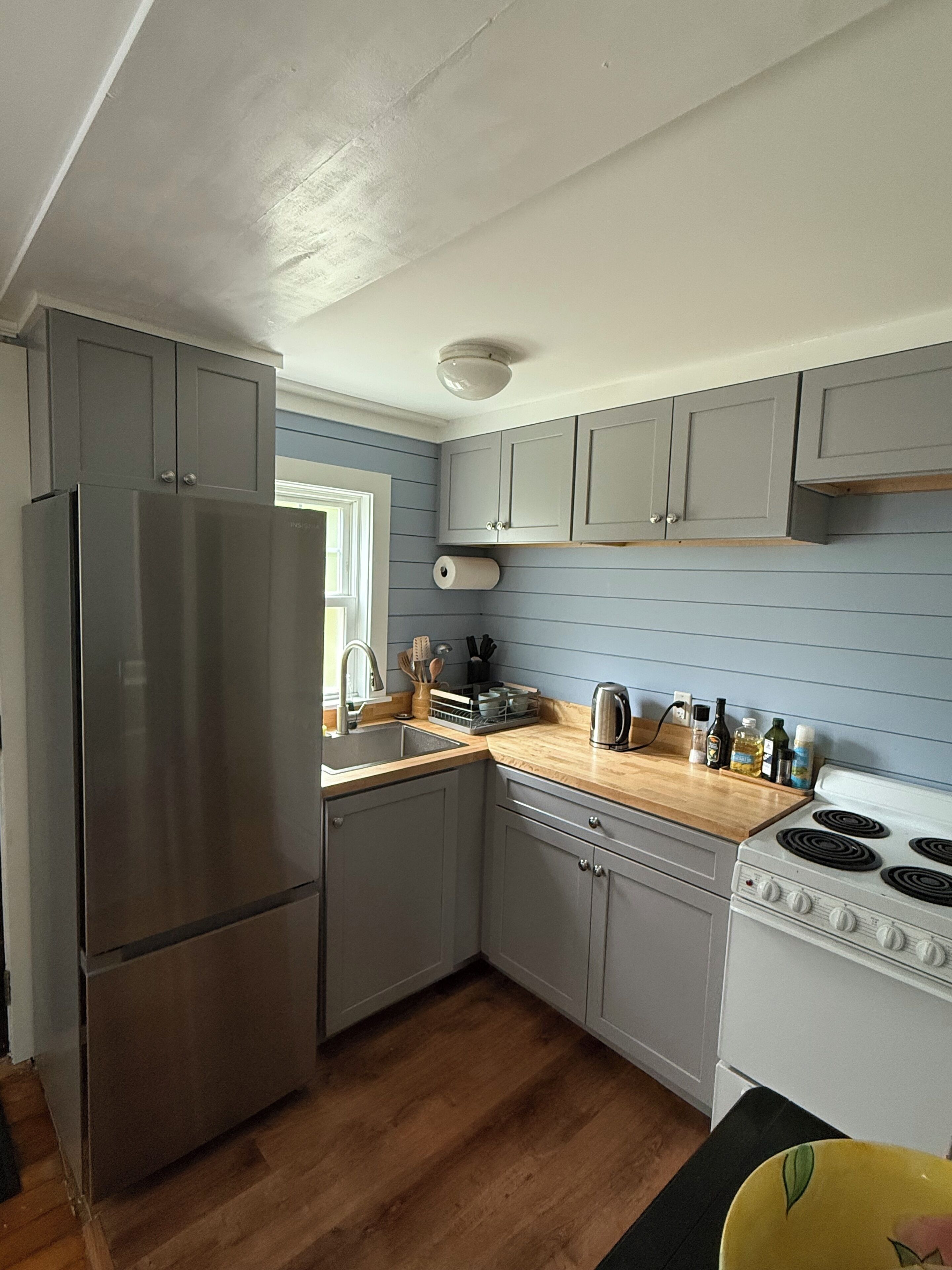 Una cocina compacta con gabinetes grises, un refrigerador de acero inoxidable, una estufa blanca y encimeras de madera.