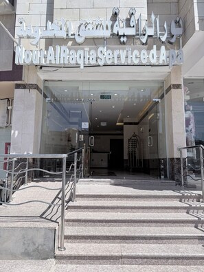 A hotel entrance with a sign in Arabic and English, a glass door, and a staircase leading up to the entrance. - Nour Al Raqia Suites (Madinah)