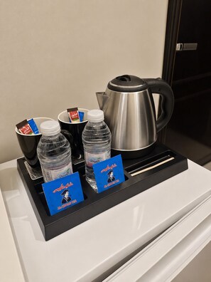 A coffee station with a stainless steel coffee pot, two cups, two bottles of water, and two packets of tea. - Nour Al Raqia Suites (Madinah)