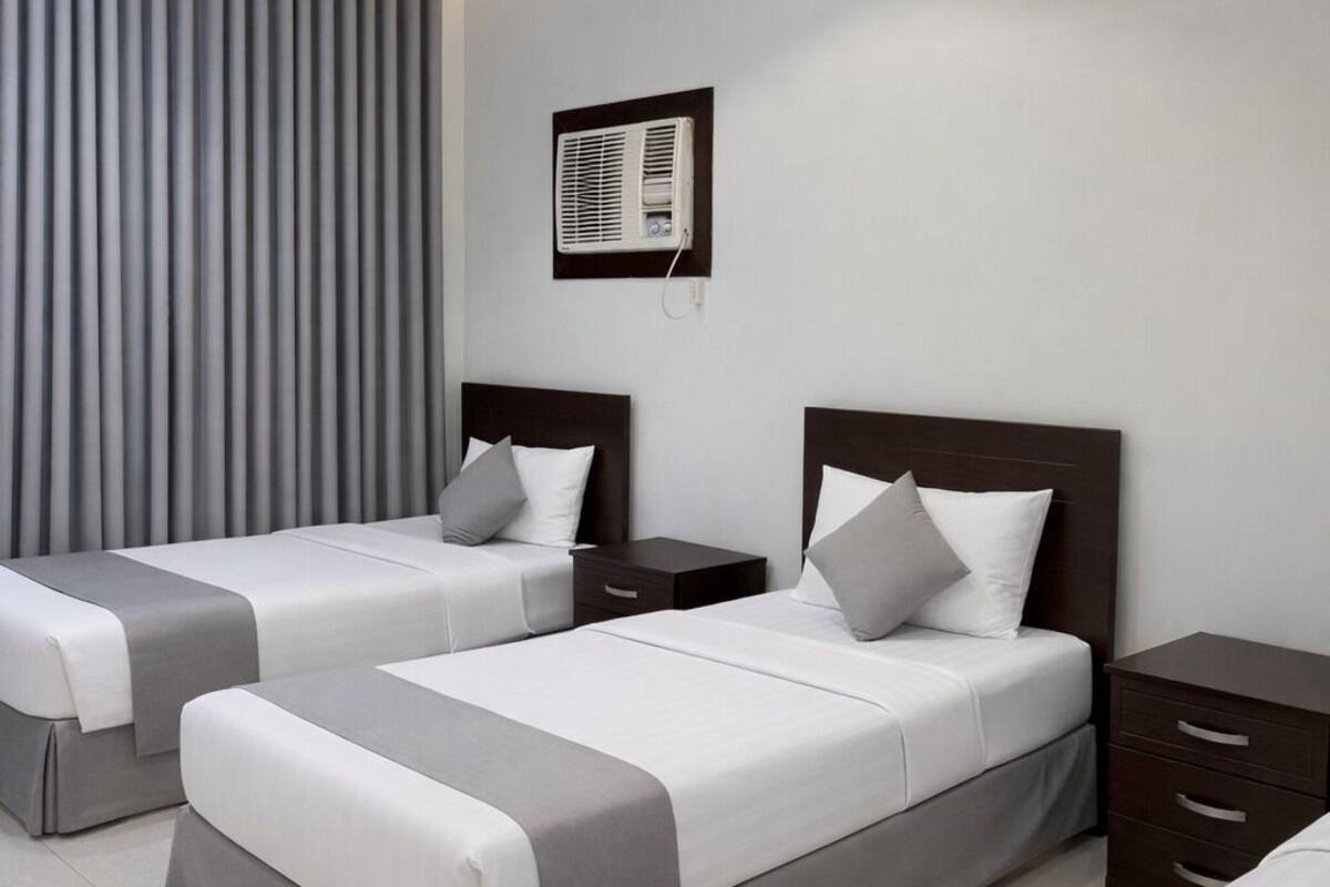 Habitació d'hotel moderna amb dos llits, aire condicionat fixat a la paret i una petita taula de nit.
