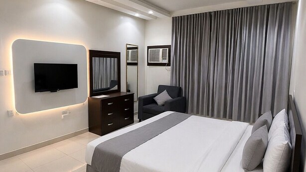 Una habitación de hotel moderna con una cama grande, un televisor de pantalla plana montado en la pared, un aparador, un espejo y una ventana con cortinas.