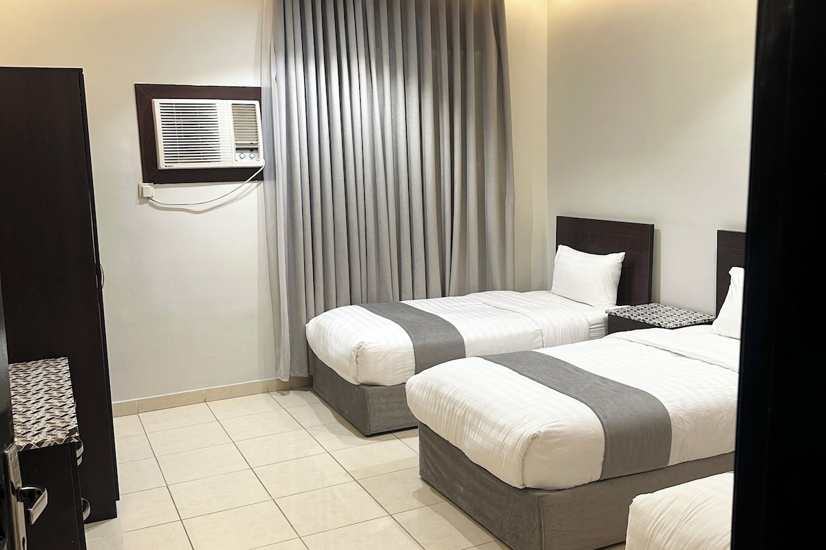 A hotel room with two beds, a built-in air conditioning unit, and a tiled floor.