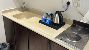 Una kitchenette con un lavamanos, estufa y cafetera. Hay dos botellas de agua y una tarjeta sobre la encimera.