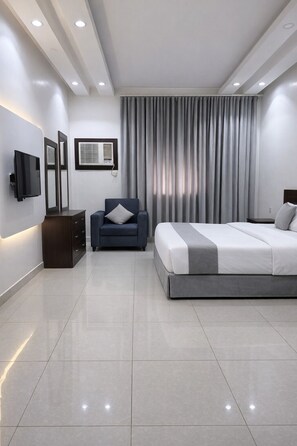 Un dormitorio moderno con cama, una silla, televisor y cómoda.