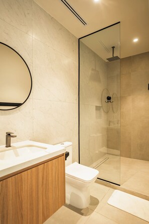 Un baño moderno con ducha envuelta en vidrio, tocador de madera y váter blanco.