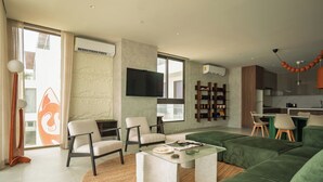 Una sala de estar moderna con un sofá verde, dos sillones, una mesa de centro y un televisor montado en la pared.