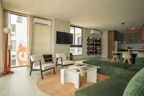 Una sala de estar moderna con un sofá verde, dos sillones, una mesa de centro y un televisor montado en la pared.