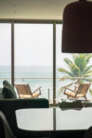Una habitación con un ventanal grande, dos sillas de mimbre, una mesita y un cojín verde.