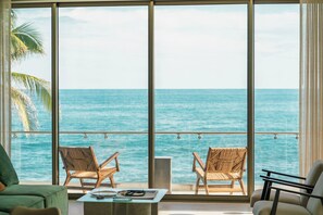 A room with a large window overlooking the ocean, two wicker chairs, a small table with a bowl and a book, and a green sofa. - Wake up to panoramic Pacific Ocean views at Solaris, a spacious oceanfront three-bedroom residence in El Zonte's Surf City. Designed for up to six guests, enjoy a private balcony, resort-style pool, high-speed WiFi, and effortless beachfront living. (Chiltiupán)