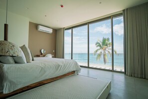 A hotel room with a large bed, a view of the ocean, and a window with curtains. - Wake up to panoramic Pacific Ocean views at Solaris, a spacious oceanfront three-bedroom residence in El Zonte's Surf City. Designed for up to six guests, enjoy a private balcony, resort-style pool, high-speed WiFi, and effortless beachfront living. (Chiltiupán)