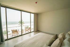 Un dormitorio con una cama grande, vistas a la playa y un balcón con sillas.