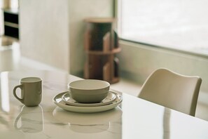 Una mesa con una taza y un plato, una silla y una ventana con vistas.