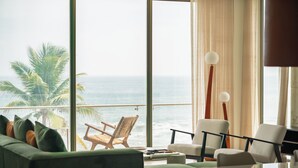 Una habitación con un amplio ventanal con vistas al océano, un sofá verde, una silla blanca y una mesa con una lámpara.